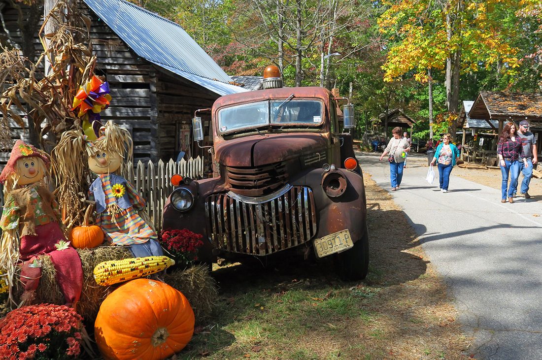 Fair attendees pass by a display of punkins surrounding an antique fire engine.