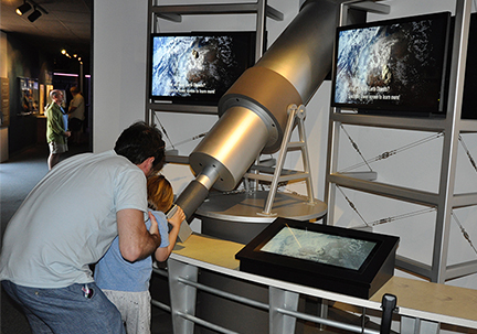 A man helps a child look through a telescope in a museum dedicated to astronomy.