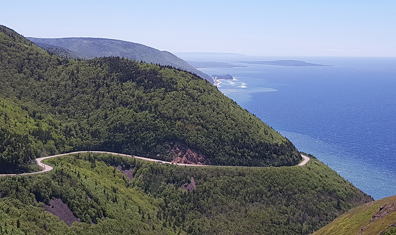 A winding road curves around a cliffside with blue water in the background.