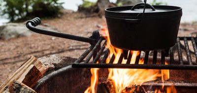 A dutch oven sits on a grill on a robust fire.
