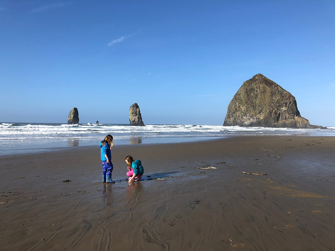 Two girls play on the beach with three big outcroppings looming in the distance.