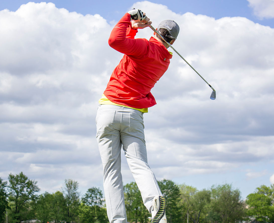 A golfer in a red jacket completes a drive.
