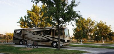 Brown and tan colored motorhome parked in driveway near trees on sunny day