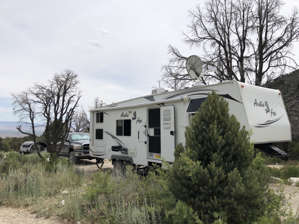 An Arctic Fox fifth-wheel at a campsite with leafless winter trees in the desert.
