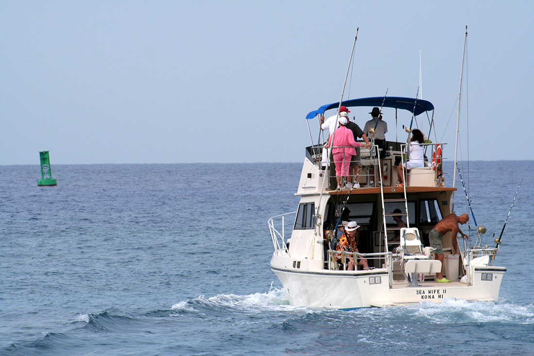 A fishing boat laden with passenger and crew heads out to the sea.