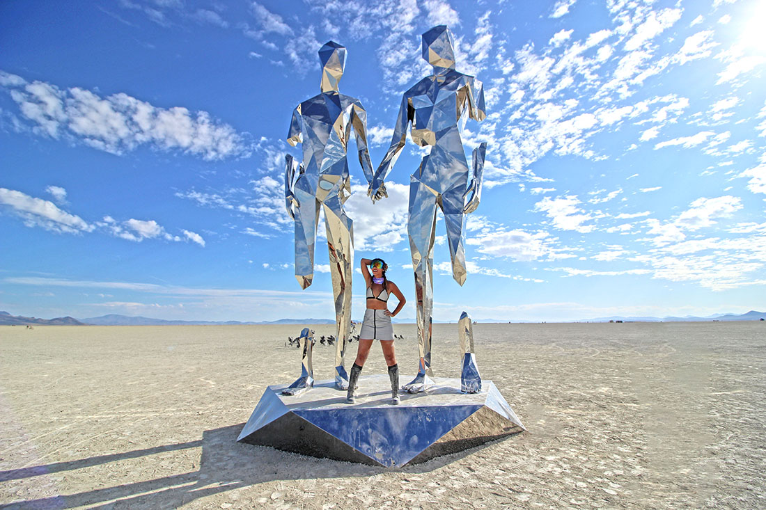 A woman in futuristic garb flanked by two reflctive statues.