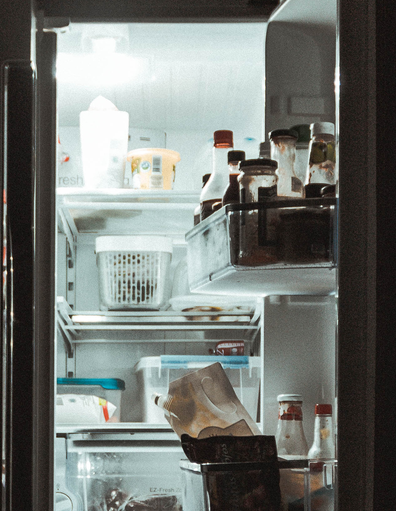 A fridge door open revealing ketchup and sauces on the door and plastic containers on the shelves. 