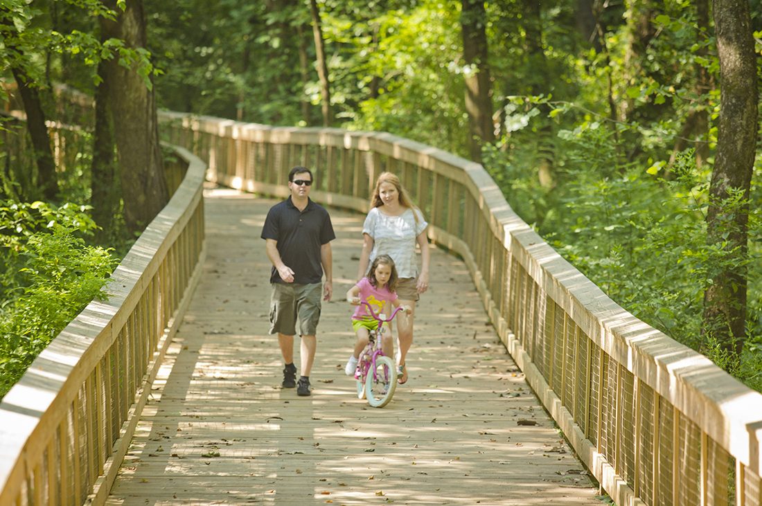 A family of three walks down a footbridge; the kid rides a bike.