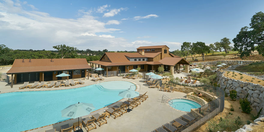 A luxury RV resort with a pool lined with deck chairs, two ranch-style buildings and a jacuzzi.
