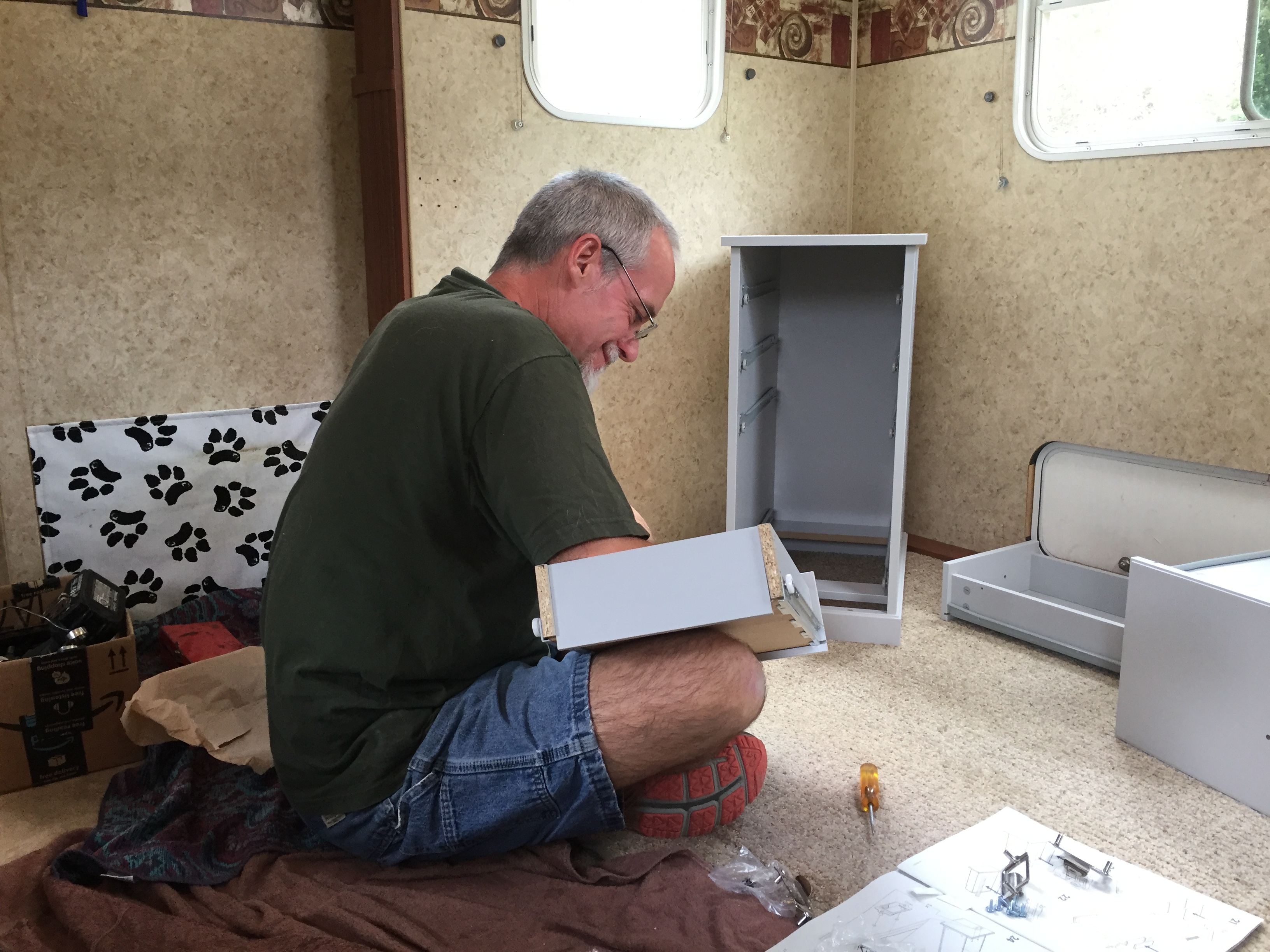 A man sitting on the floor assembling drawers for a cabinet.