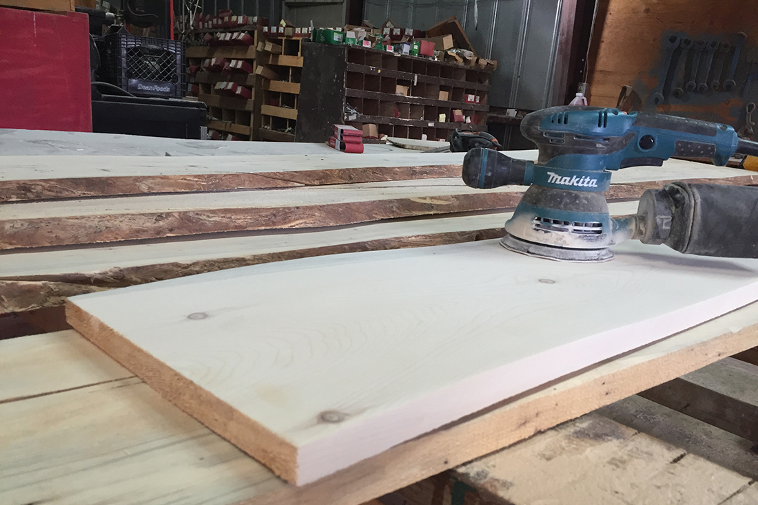 A Makita sander at rest atop a flat piece of wood in a workshop.