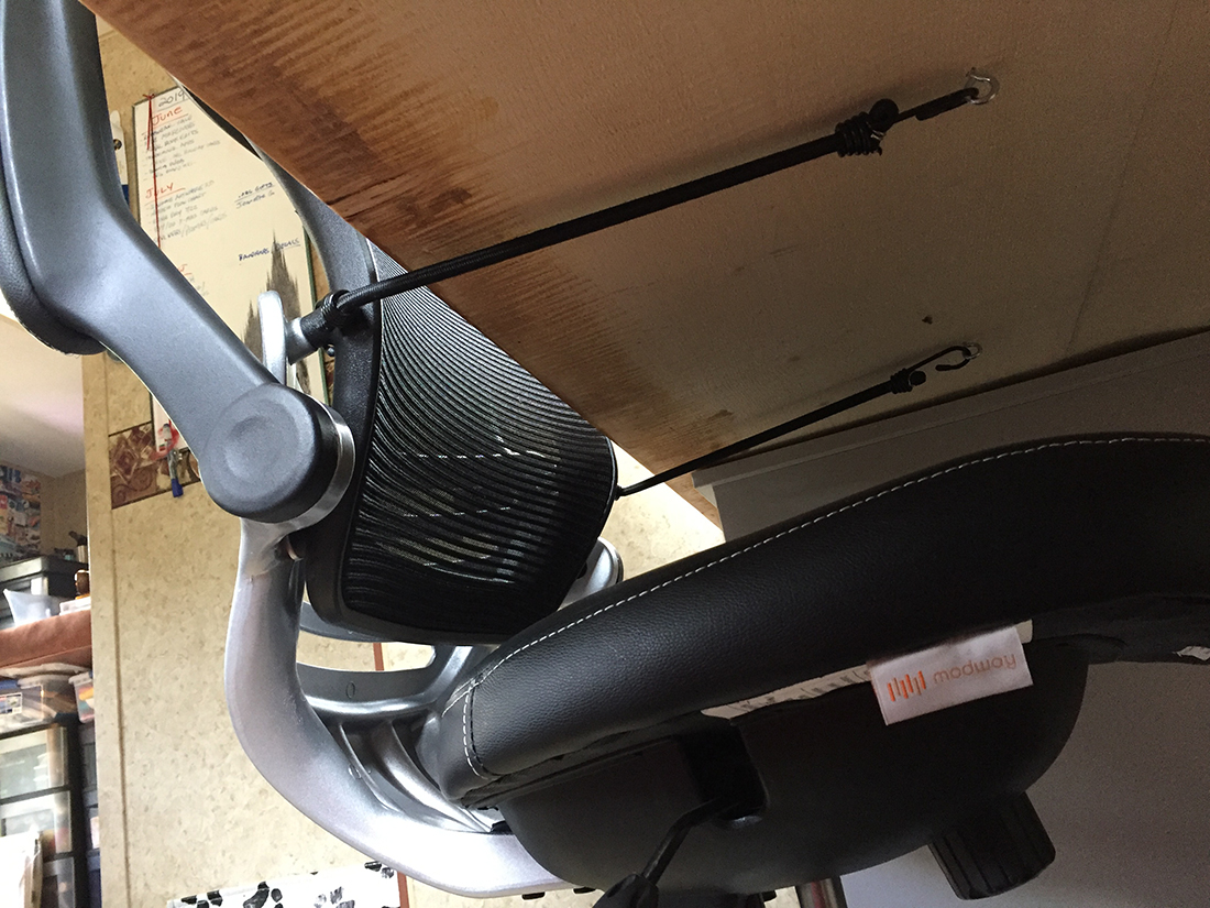 POV from under a desk, a chair secured to a desk with bungee cords and eye bolts.