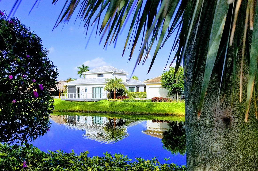 Small homes over look a canal flanked by lush green banks and palm trees.