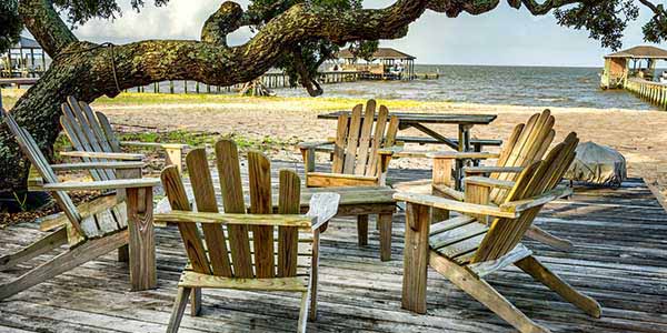 Four Adirondack chairs on a wooden deck near the water.