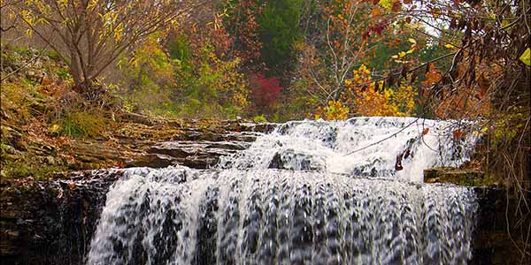A waterfall among the waning colors of Autumn at the Tanyard Creek Park Nature Trail in Bella Vista, AR.