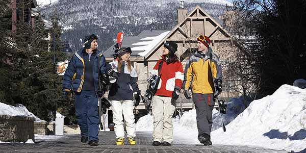 Four adults with skis and snowboards walking and talking