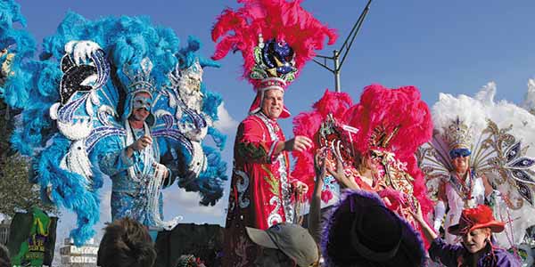 People in Mardi Gras robes with feathery headdresses cavort on a stage.