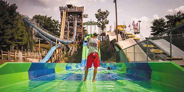 Lifeguard watches over a wide green waterslide.