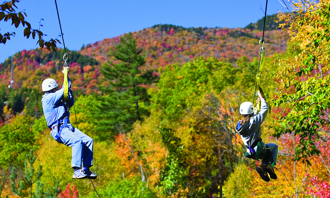 A senior man and a young woman zipline with fall foliage in the background.