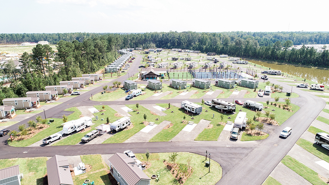 An aerial view of an RV park with neat concrete spaces and bordered with pine trees.