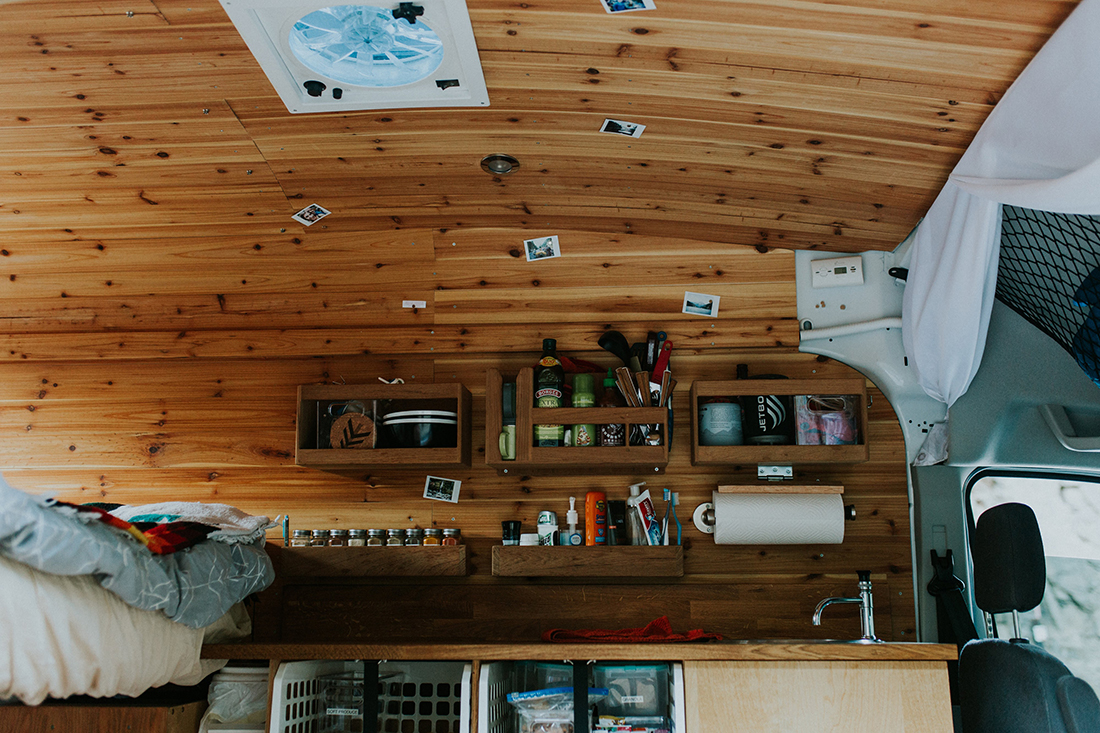 A camper van interior festooned with photos and appointed with shelves containing household items.