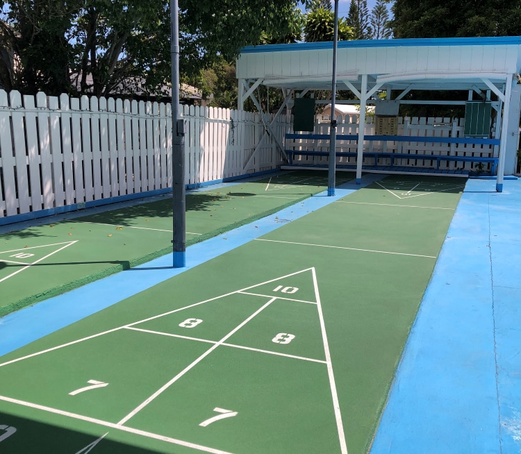 Two shuffleboard courts running parallel to a wooden picket fence.