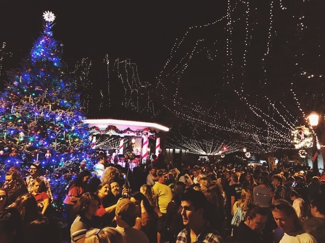 A crowd of revelers celebrate outdoors under a Christmas tree festooned with blue lights.