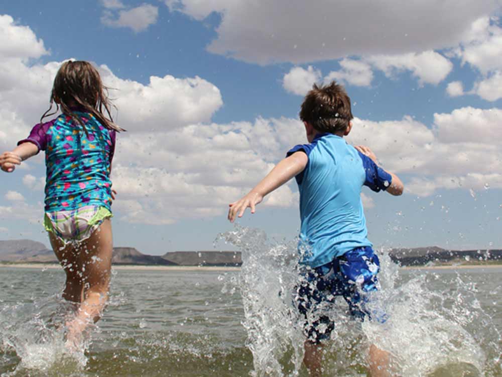 Two children bound into a lake with desert buttes in the background.