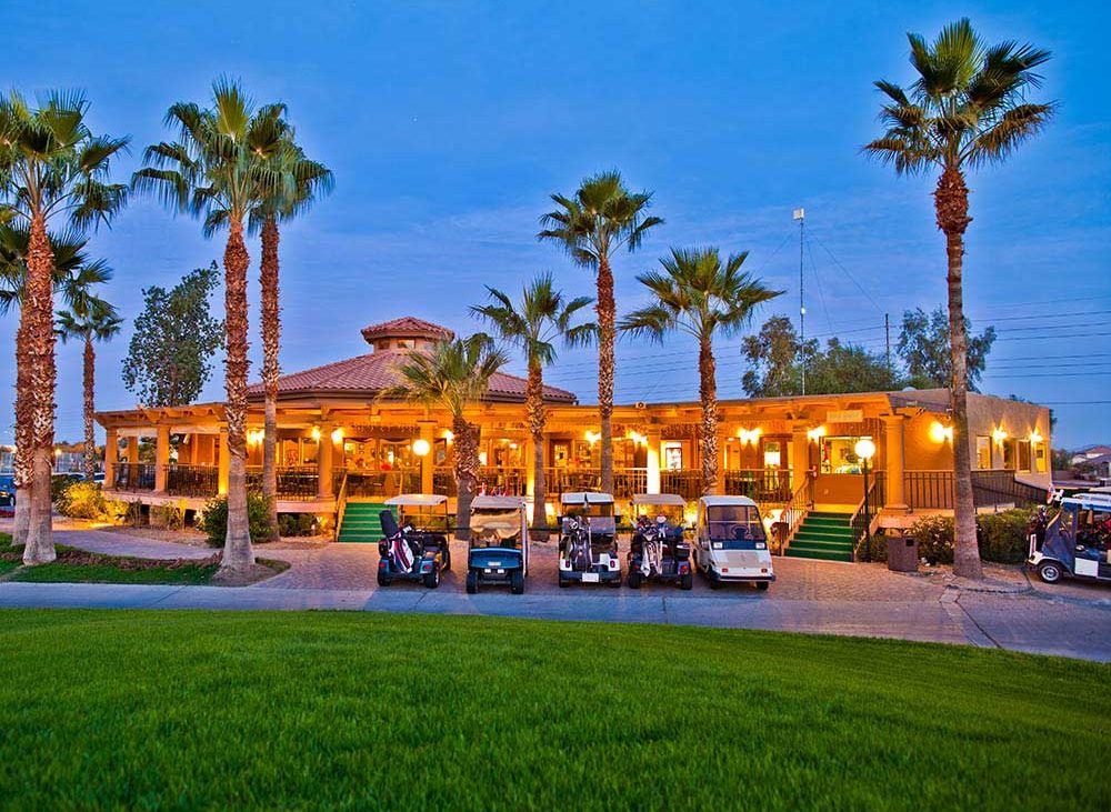An Arizona resort under tall palms turns on its light as dusk descends.