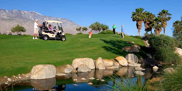 Lady grabbing golf clubs from golf cart in a desert setting.