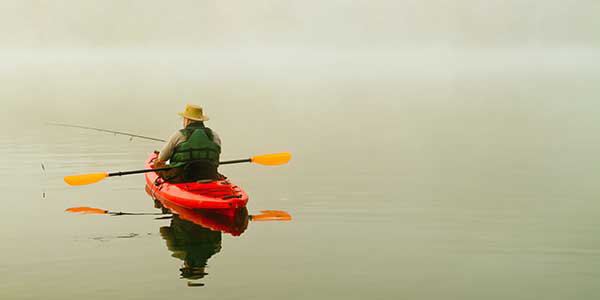 A man in a red kayak lowers his fishing line into the water.