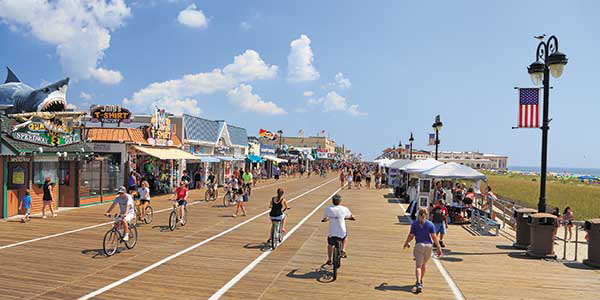 Cyclists ride down a boardwalk lined by quirky storefronts.