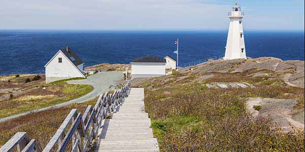 A wooden stairway leads down to a white lighthouse and ocean beyond.