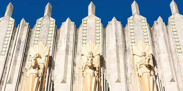 Three statues of haloed goddesses stand in front of an art-deco structure in Tulsa.