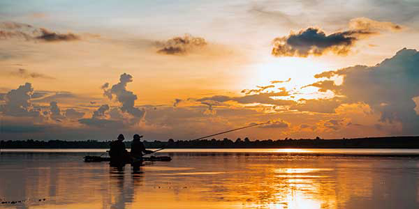 Two people on kayaks fish on a vast, calm lake during sunset.