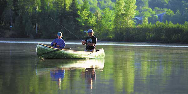 Two men fishing on a river in a green canoe.