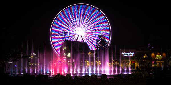 A Ferris wheel lit up in candy colors spins in the night.