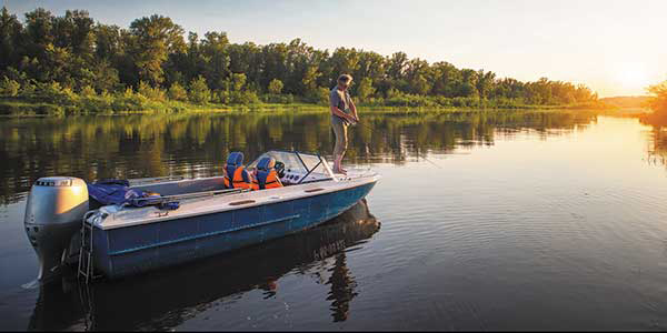Standing on his boat, an angler reels in a line in a lake.
