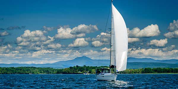 A sailboat skims across blue water with green banks in the background.