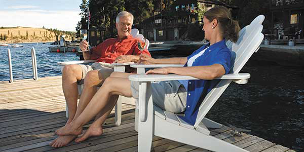 A man and woman lounge on a dock in Adirondack chairs.