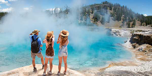 Three women raise cameras to take photos of steaming hot springs.
