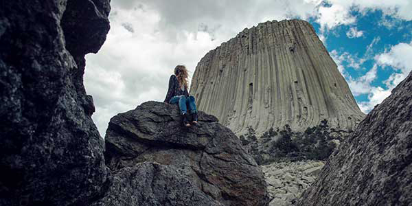 Woman looks up at Devil's tower, which resembles big smokestack.
