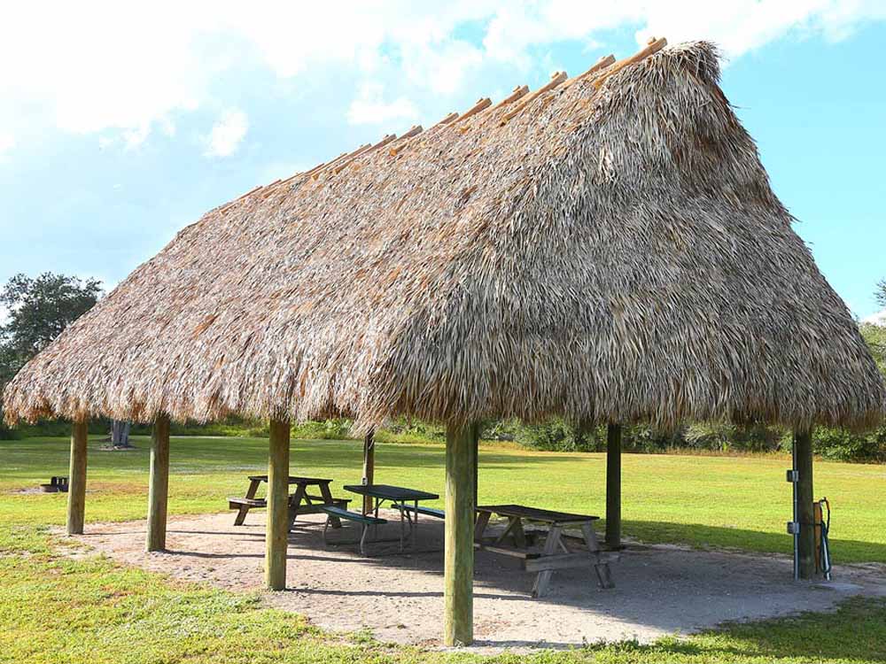 A chickee hut casts shade on a picnic bench.