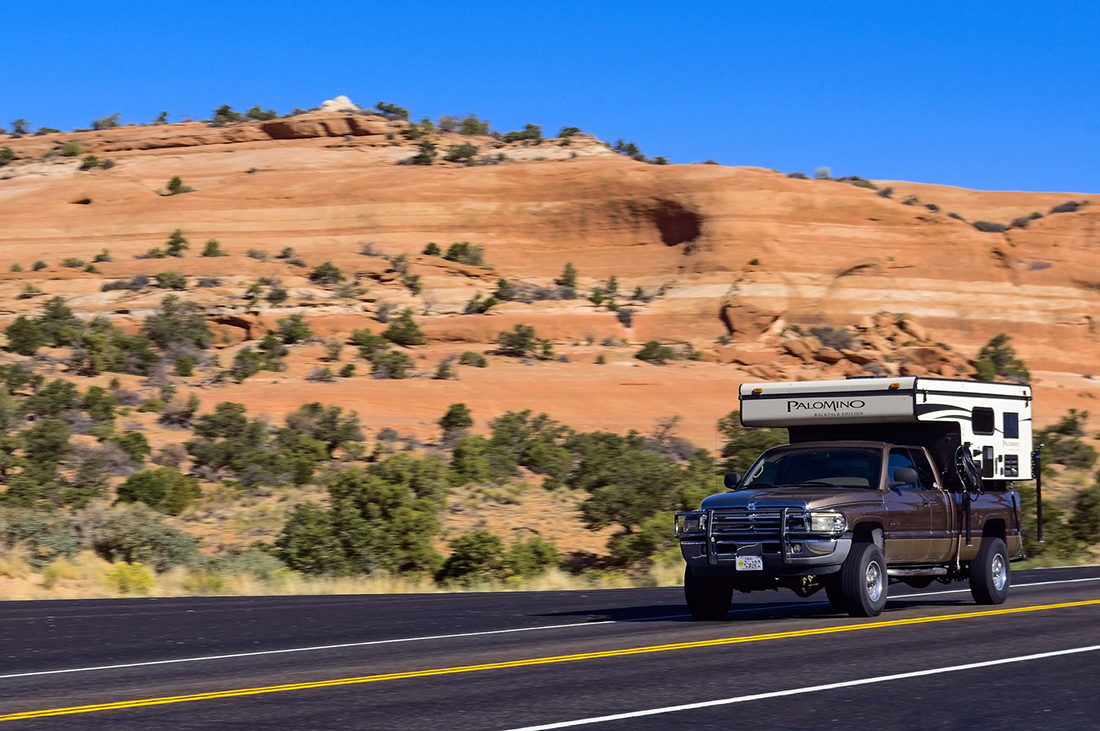 A truck camper motors through a desert landscape.