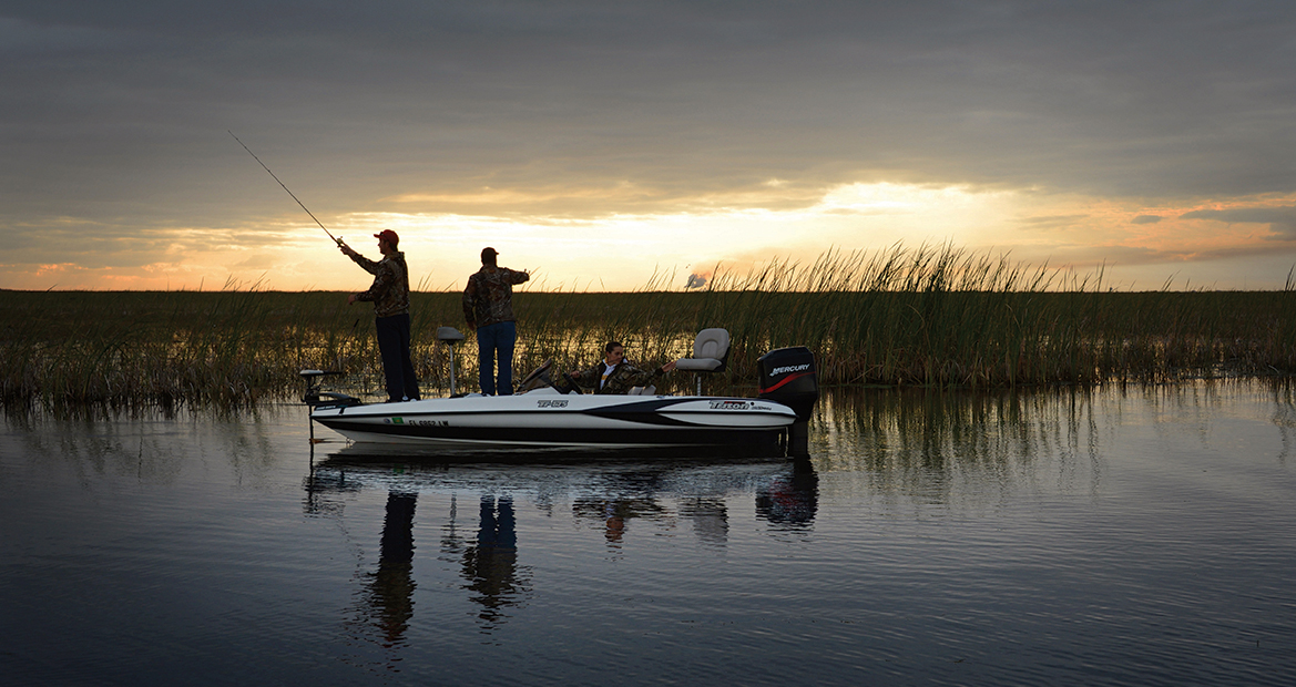 Two men fish on a boat under dawn light. 