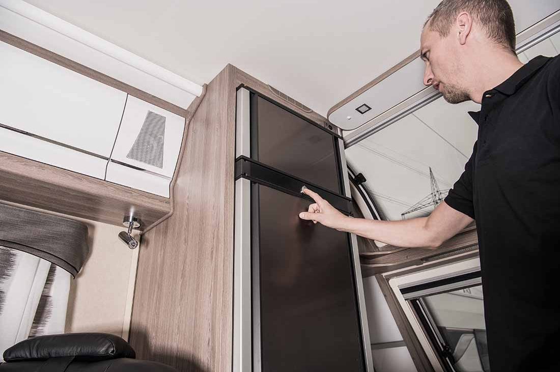replacing RV refrigerator — man checks tall, thing fridge in motorhome.