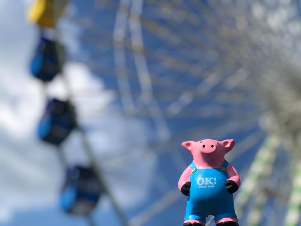 Toy pig wearing overalls in front of ferris wheel at OKC Fair