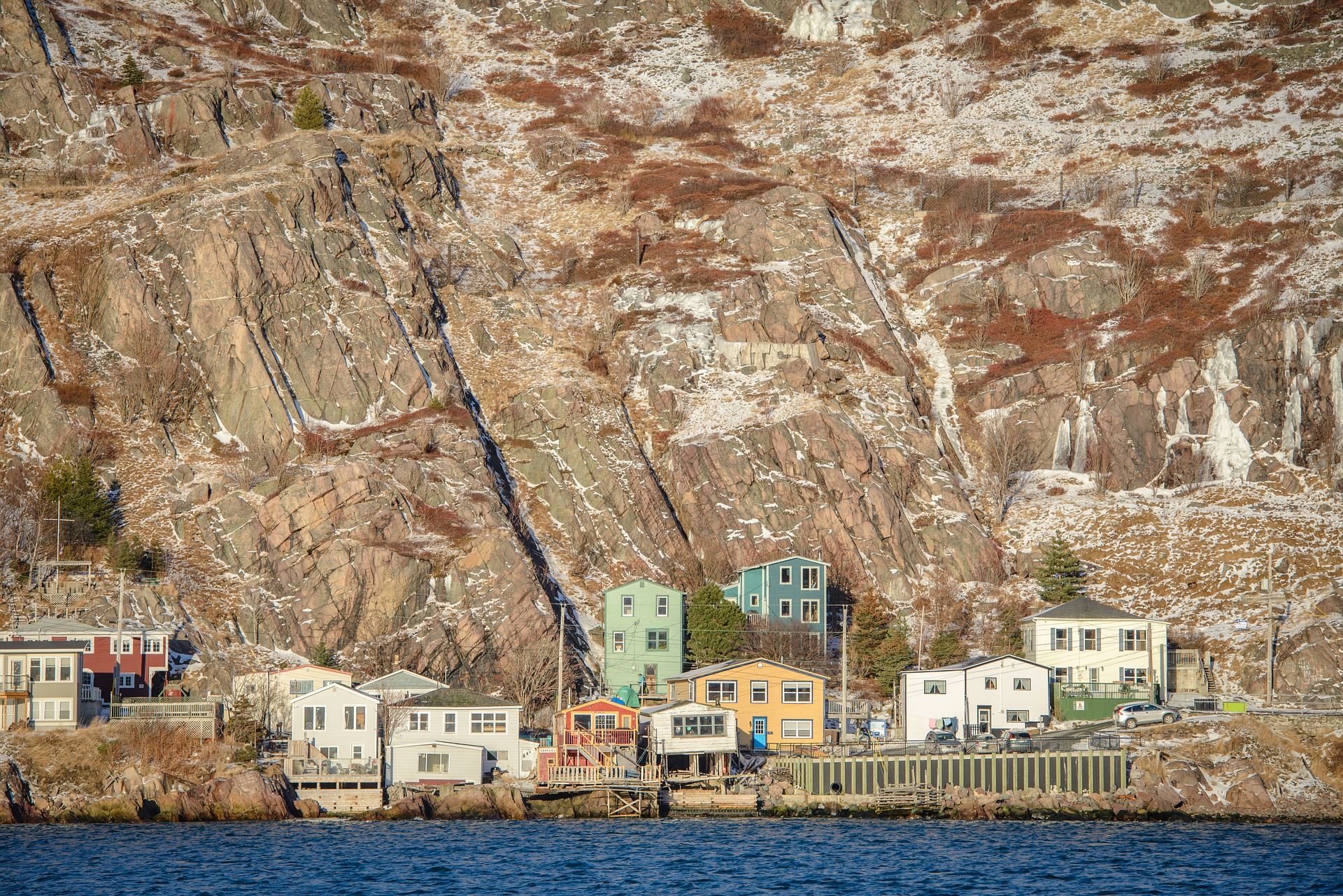 Houses occupy a thin strip of coast against a vertical cliff.