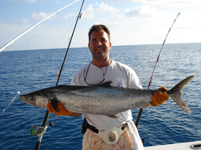A man proudly holds a hefty fish in his hands on a boat.