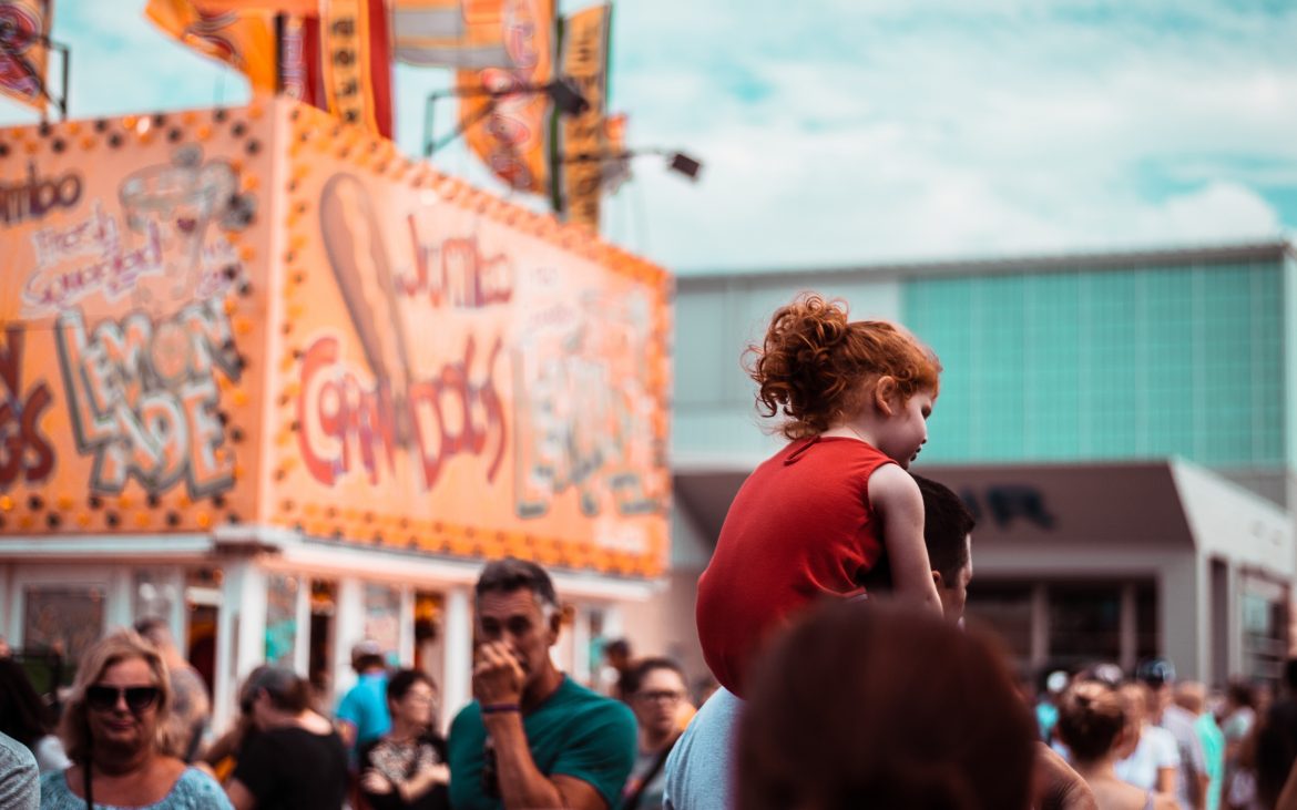 Young daughter with red hair on Dad's shoulders at OKC Fair, walking in crowd
